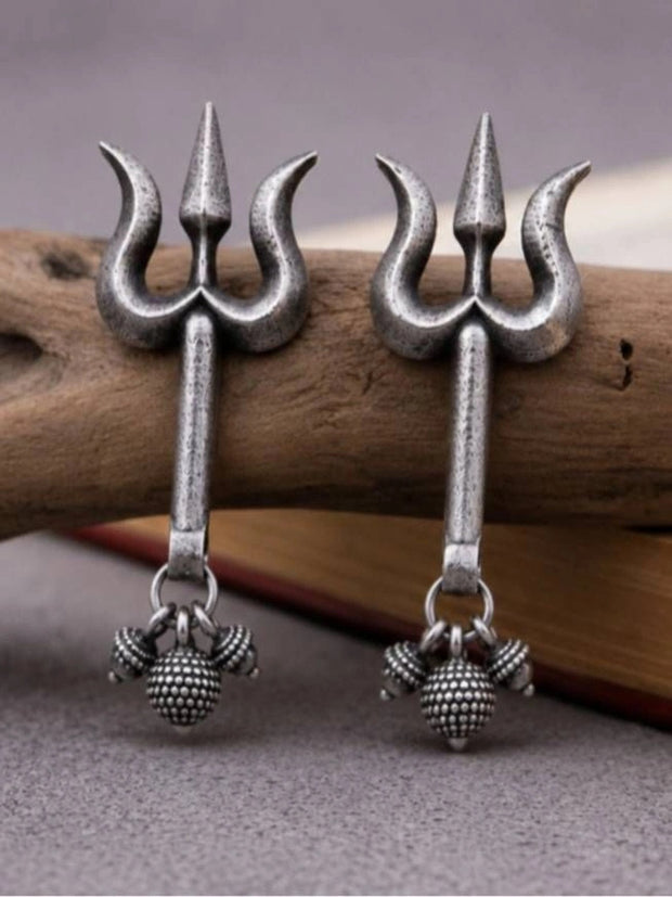 Pair of oxidised silver trishul dangler earrings with ghungroo beads resting against driftwood