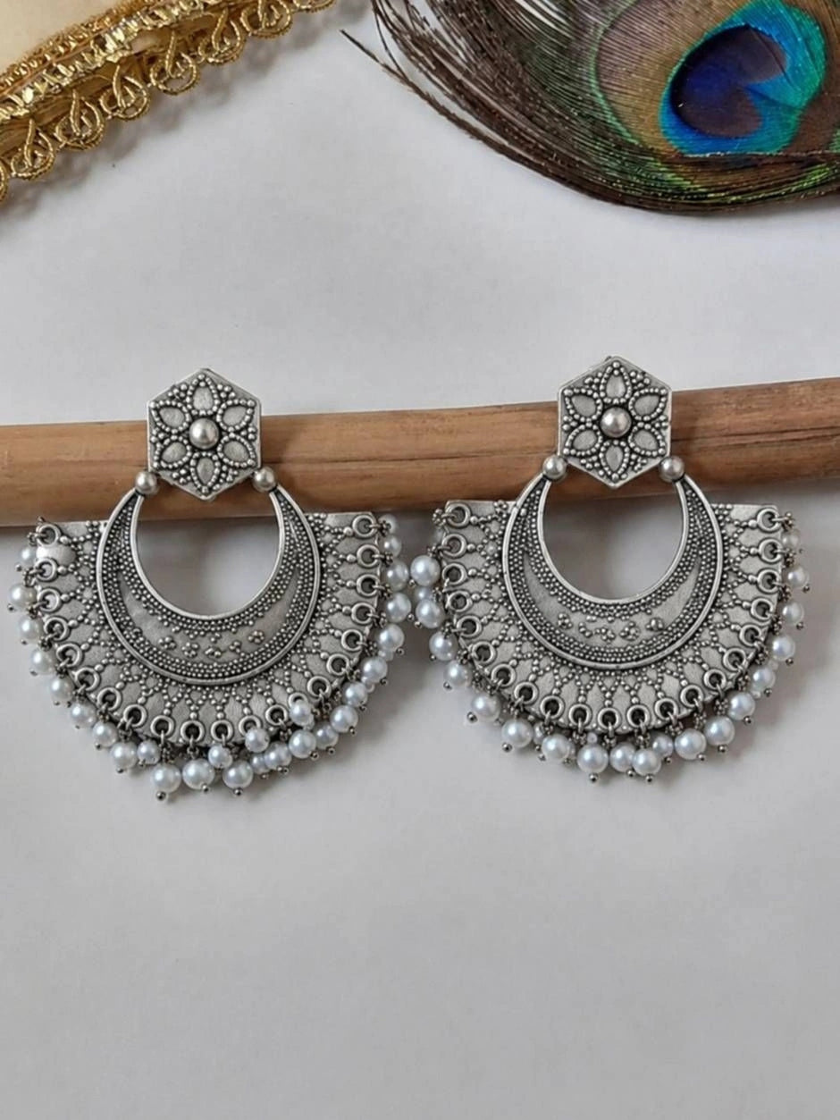 Pair of oxidised silver chandbali earrings with pearl drops resting on a wooden rod against a white background