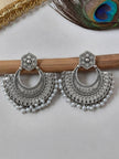 Pair of oxidised silver chandbali earrings with pearl drops resting on a wooden rod against a white background