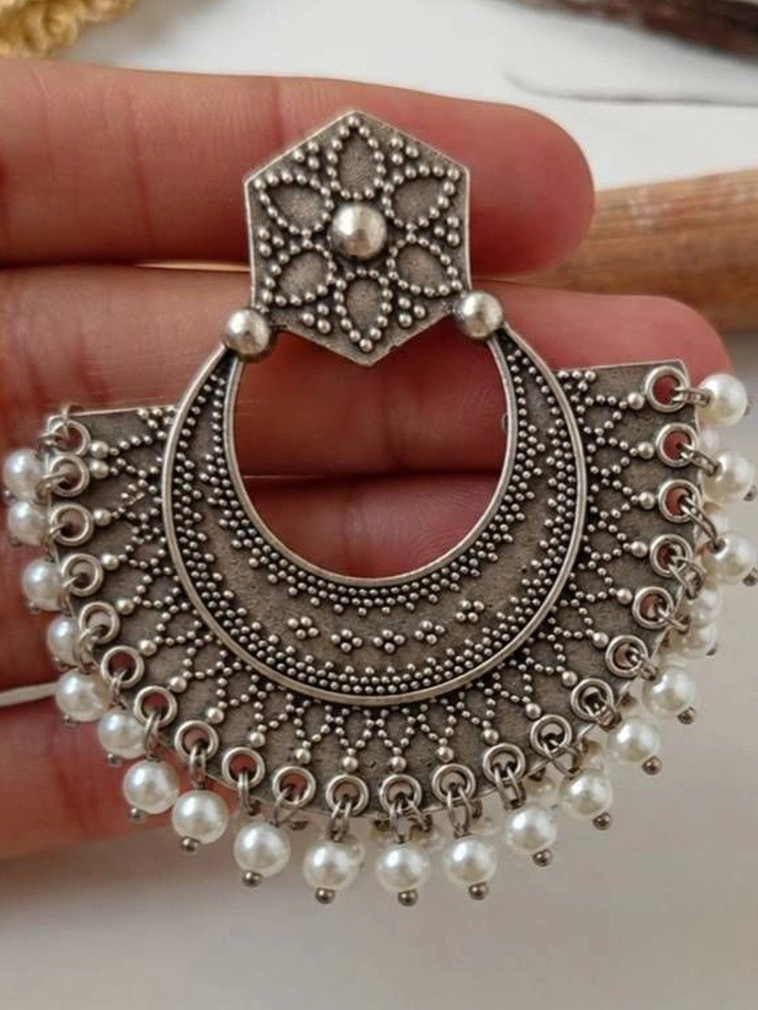 Close-up of a single oxidised silver chandbali earring held in hand revealing intricate crescent motifs and pearl drops