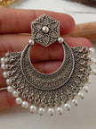 Close-up of a single oxidised silver chandbali earring held in hand revealing intricate crescent motifs and pearl drops