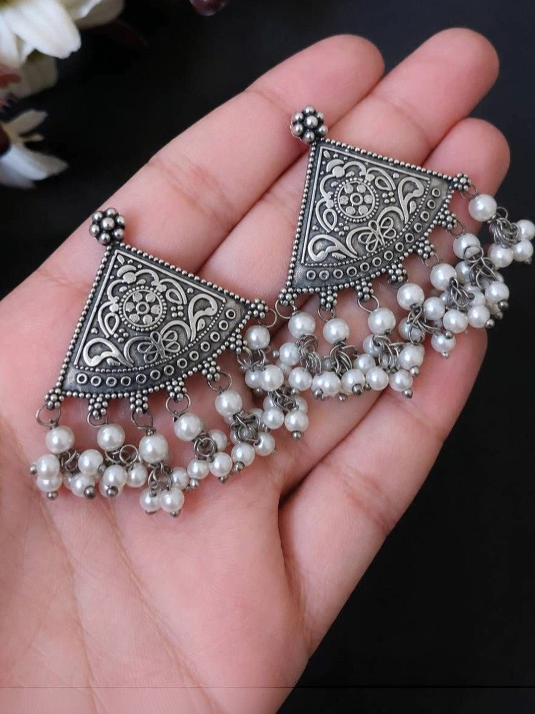 Pair of oxidised silver triangular drop earrings with cascading pearl beads resting on an open palm