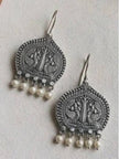 Two oxidised silver peacock earrings with pearl drops laid flat on a white textured surface