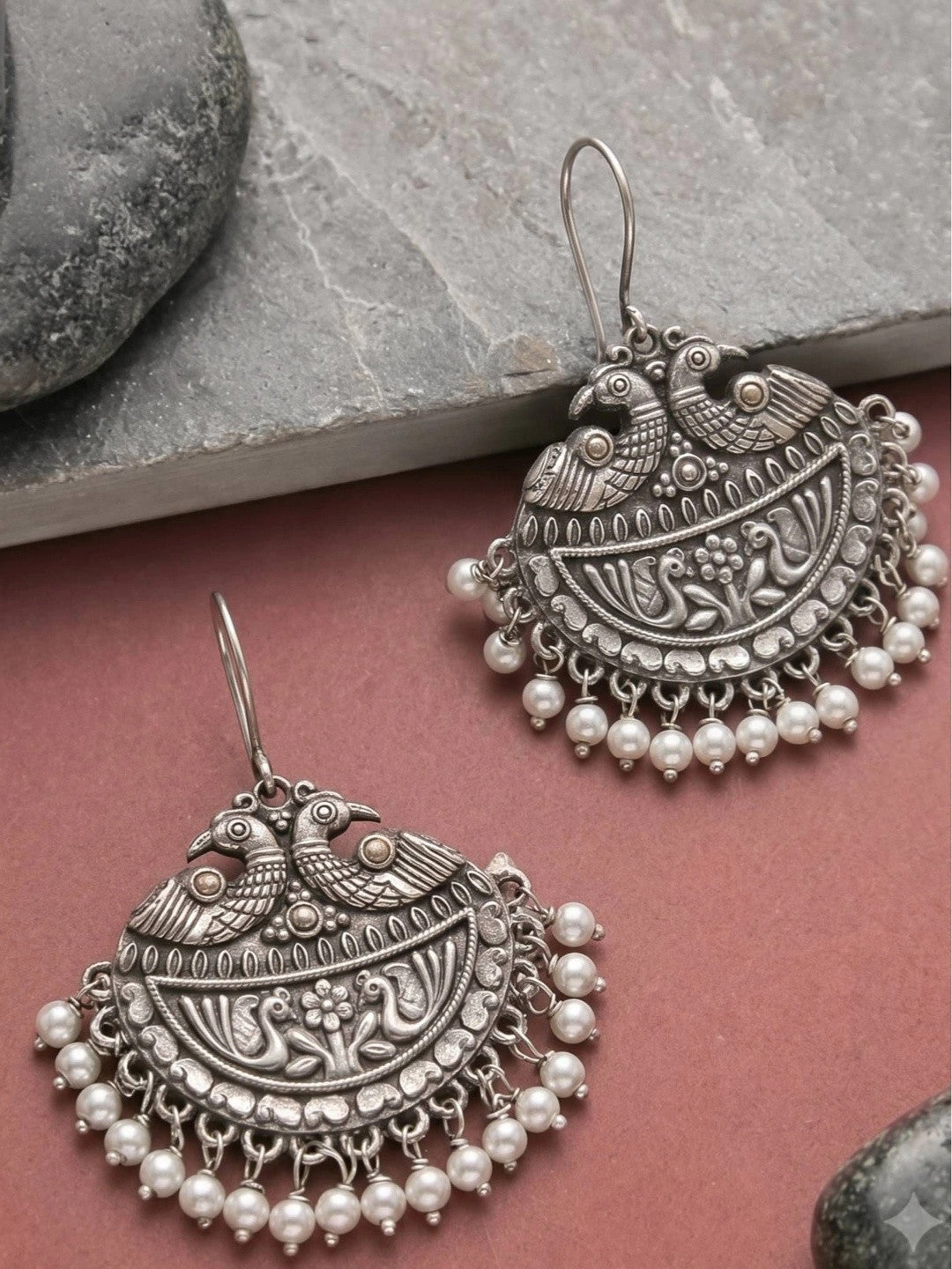Two oxidised silver chandbali earrings with pearl drops displayed on stone and pink surface showing front detail
