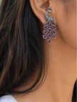 Oxidised silver peacock drop earring worn on woman's ear against dark hair