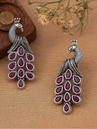 Pair of oxidised silver peacock earrings with ruby-red stones displayed on beige fabric