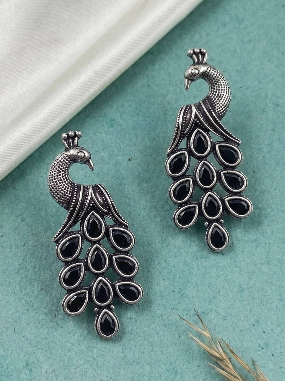 Pair of oxidised silver peacock drop earrings with black teardrop stones on teal surface