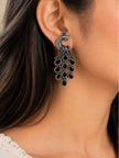 Oxidised silver peacock drop earring worn on a woman's ear against dark hair