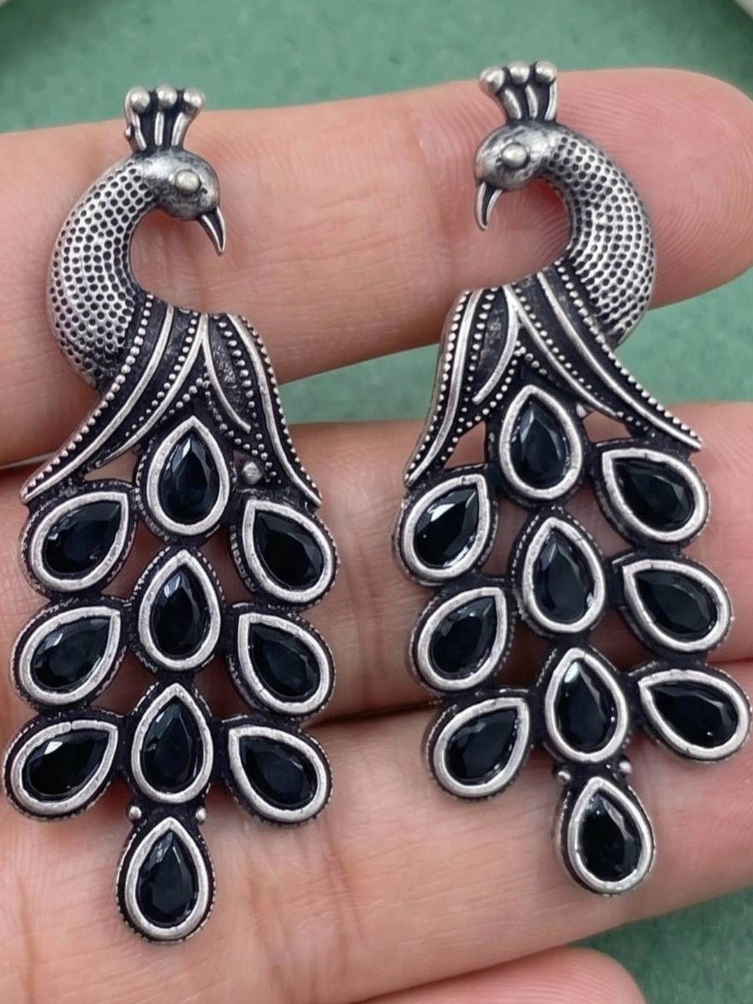 Close-up of peacock earring pair held in palm showing black stone tail detail