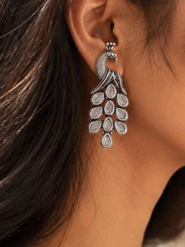 Oxidised silver peacock drop earring worn on a woman's ear showing full cascading mirror tail