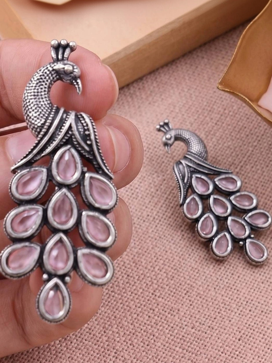 Hand holding large oxidised silver peacock earring beside smaller variant showing size comparison