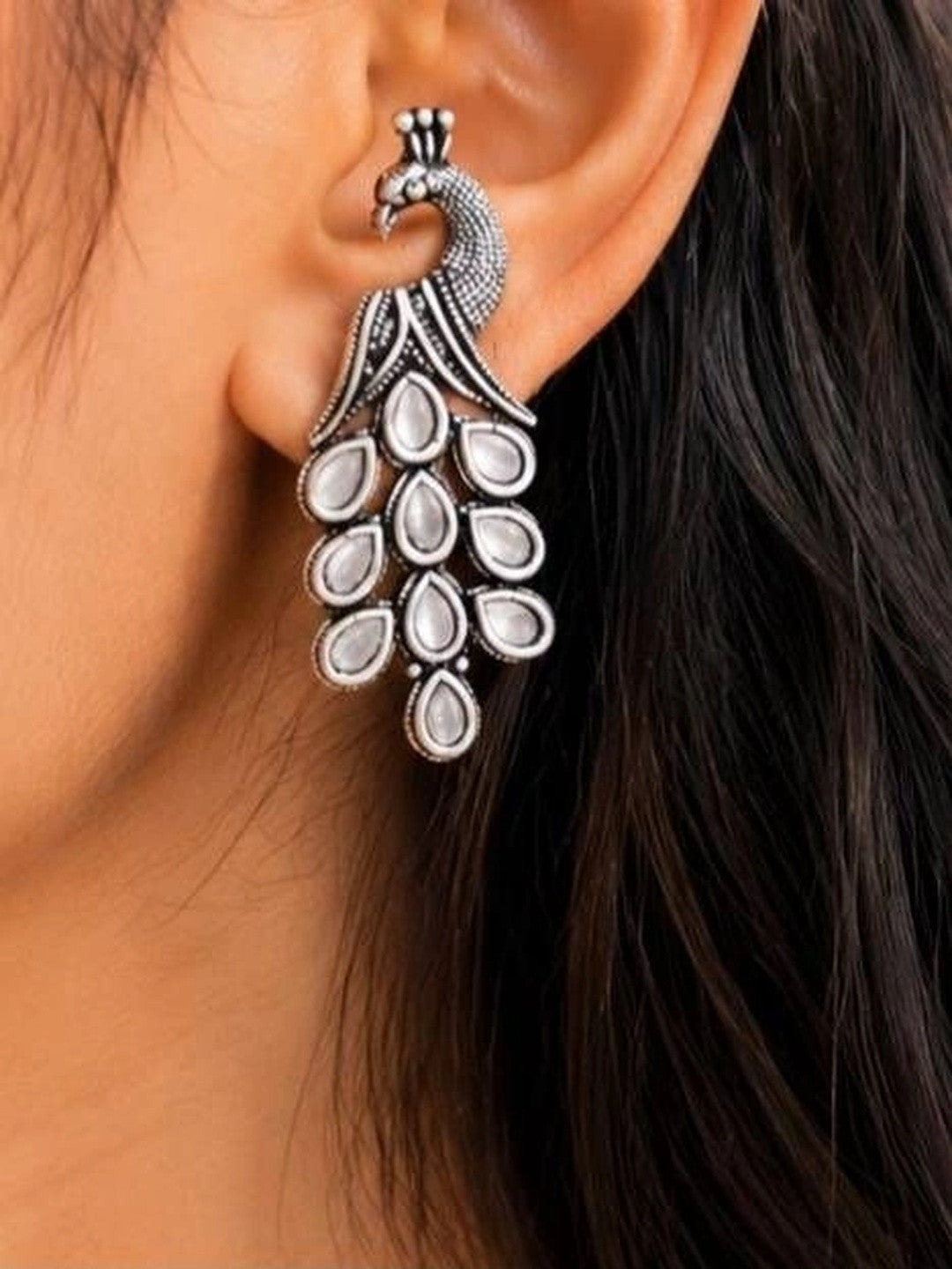 Oxidised silver peacock drop earring worn on ear showing full length and crested peacock head detail