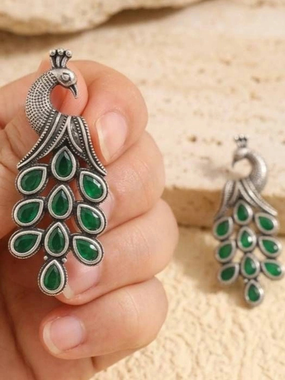 Hand holding a large oxidised silver peacock earring with green teardrop stones cascading as the tail