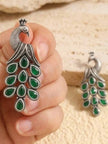 Hand holding a large oxidised silver peacock earring with green teardrop stones cascading as the tail