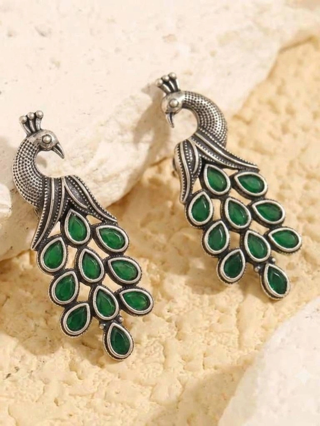 Pair of oxidised silver peacock earrings laid flat on a cream textured surface showing mirrored design