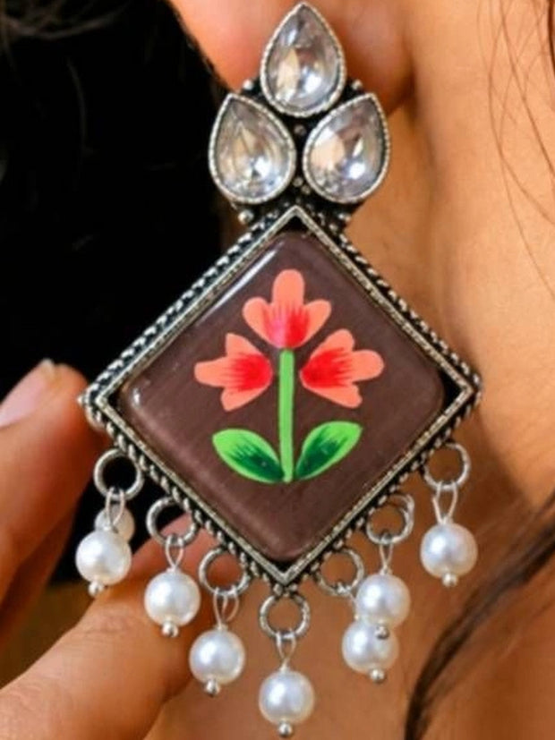 Close-up of one oxidised silver drop earring with coral meenakari flower and pearl drops held near a woman's ear