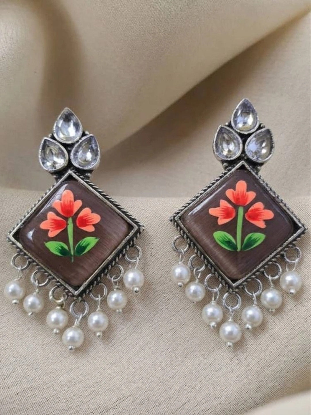 Pair of oxidised silver meenakari drop earrings laid flat on a cream fabric background