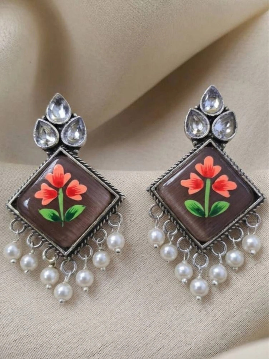 Pair of oxidised silver meenakari drop earrings laid flat on a cream fabric background