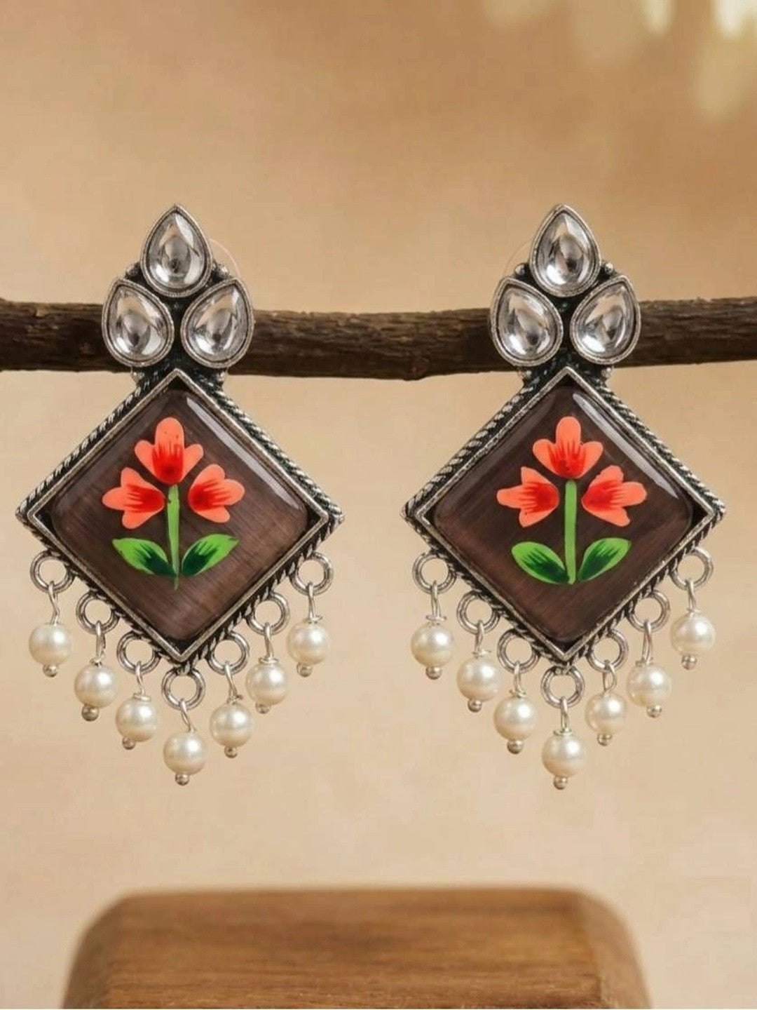 Both earrings hanging from a wooden branch showing the full diamond shape and pearl fringe