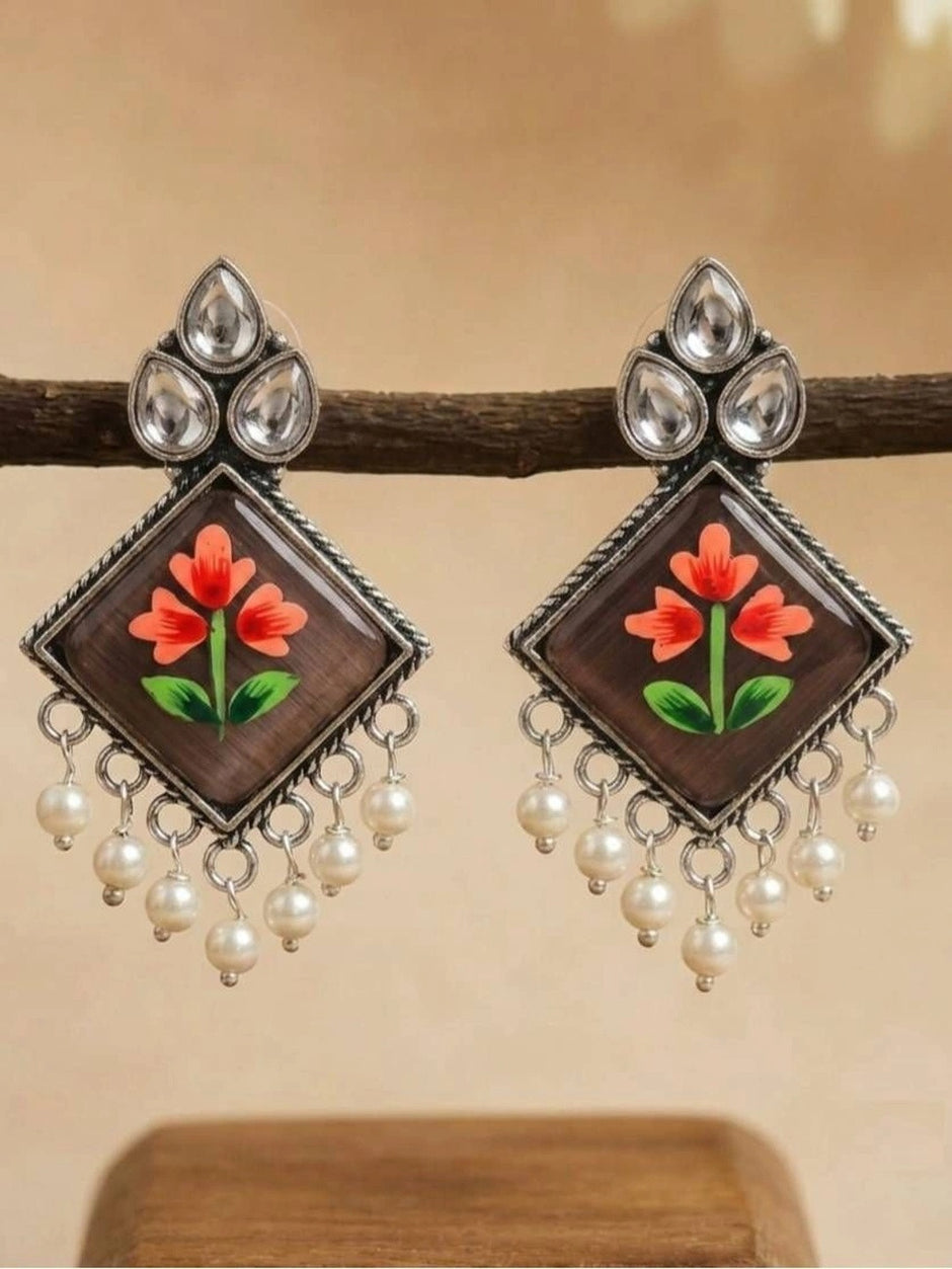 Both earrings hanging from a wooden branch showing the full diamond shape and pearl fringe