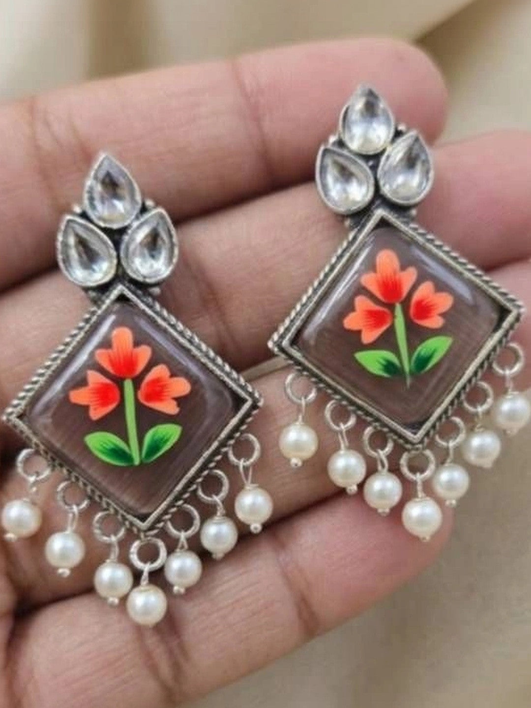 Pair of floral meenakari drop earrings with ivory pearl drops resting on an open palm