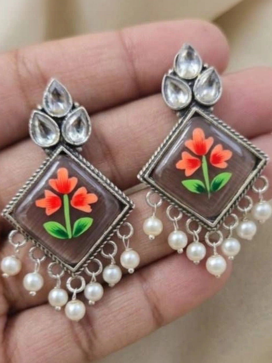 Pair of floral meenakari drop earrings with ivory pearl drops resting on an open palm