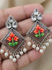 Pair of floral meenakari drop earrings with ivory pearl drops resting on an open palm