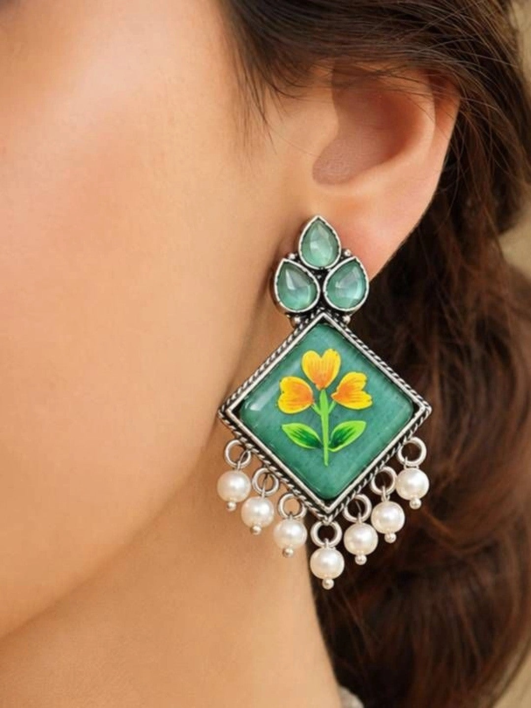 Woman wearing oxidised silver minakari floral drop earring with green enamel tile and pearl drops