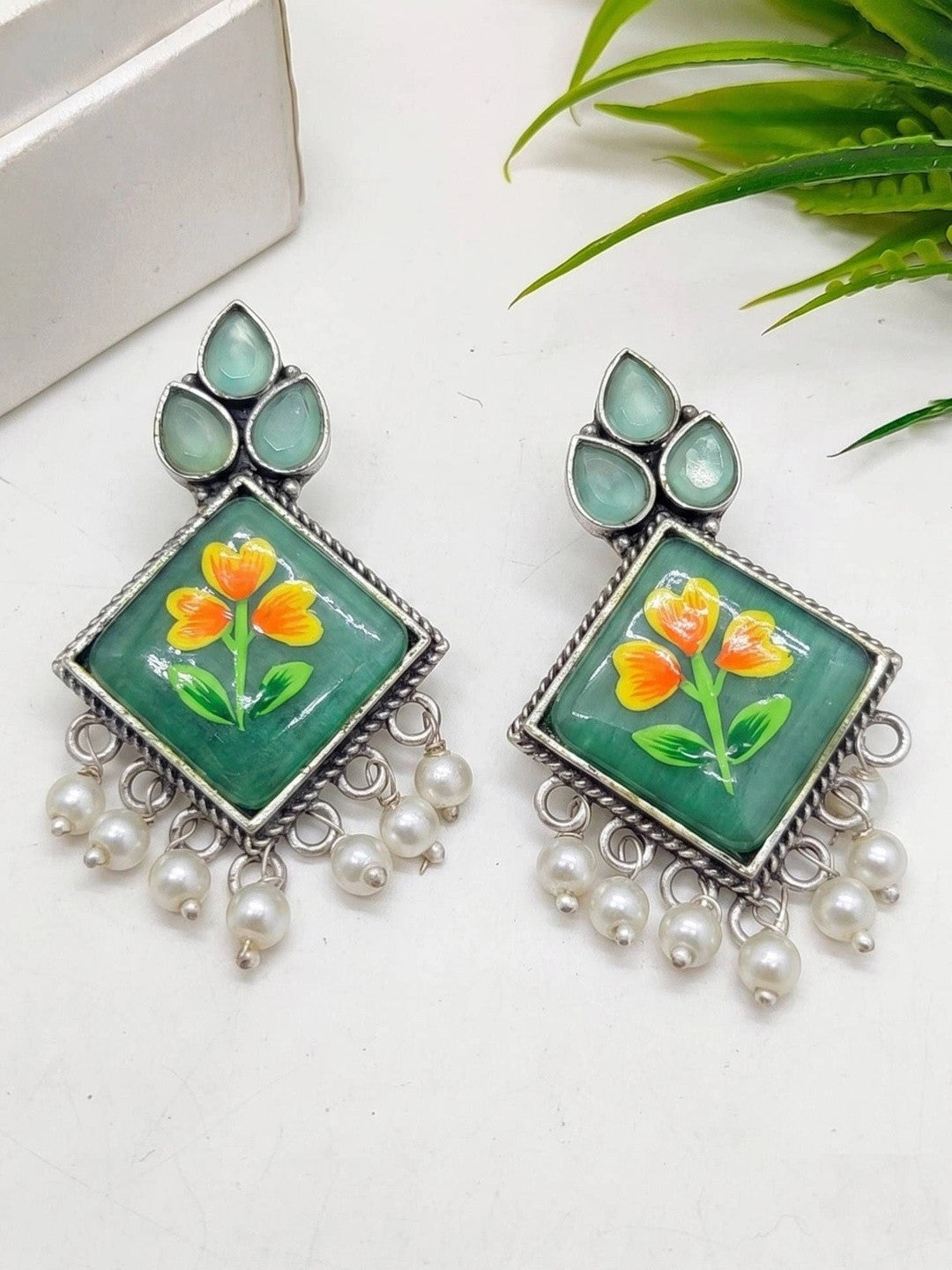 Pair of oxidised silver minakari earrings with orange floral enamel and white pearl drops laid flat
