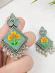 Close-up of one minakari floral earring held in hand showing enamel detail and pearl drops