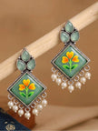 Pair of oxidised silver floral minakari earrings displayed on a wooden rod against warm background