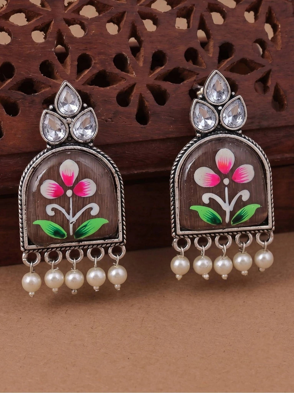 Pair of oxidised silver arch jhumka earrings with hand-painted pink flower on wooden background
