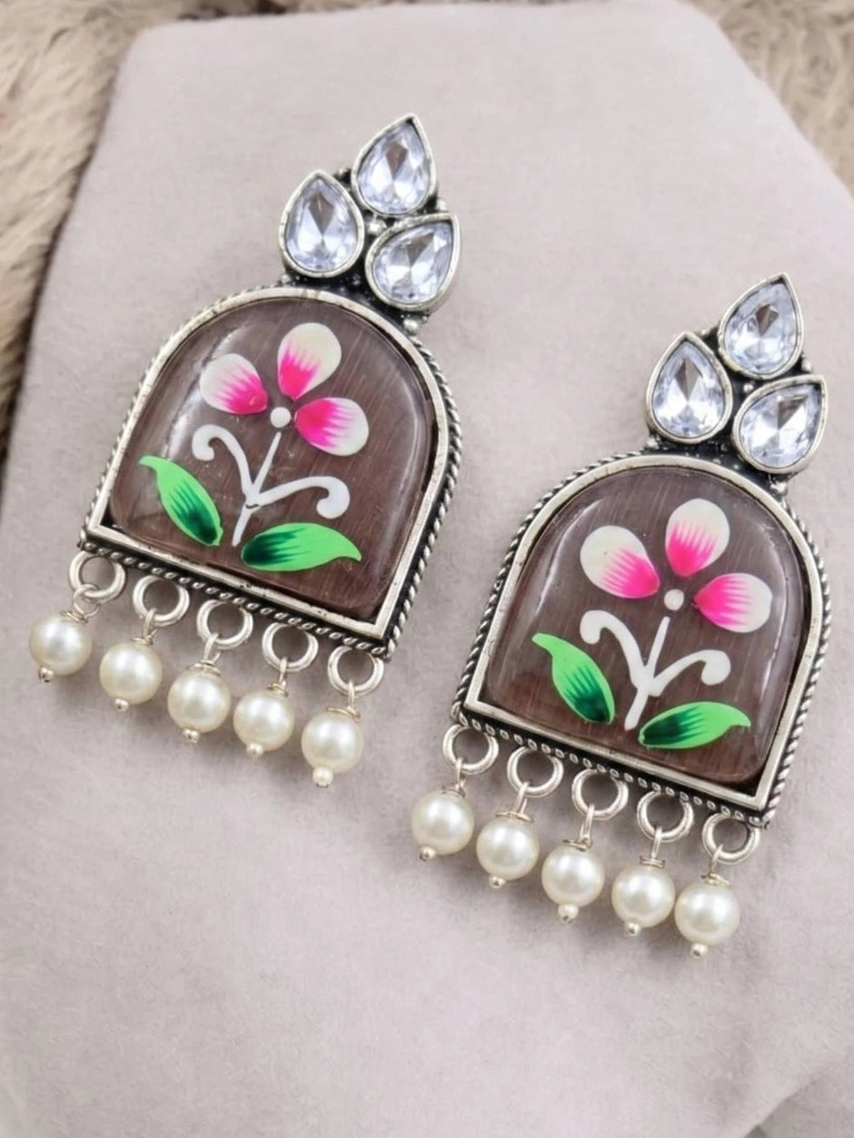 Two floral painted jhumka earrings with crystal teardrops and faux pearl drops on grey surface