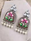 Two floral painted jhumka earrings with crystal teardrops and faux pearl drops on grey surface