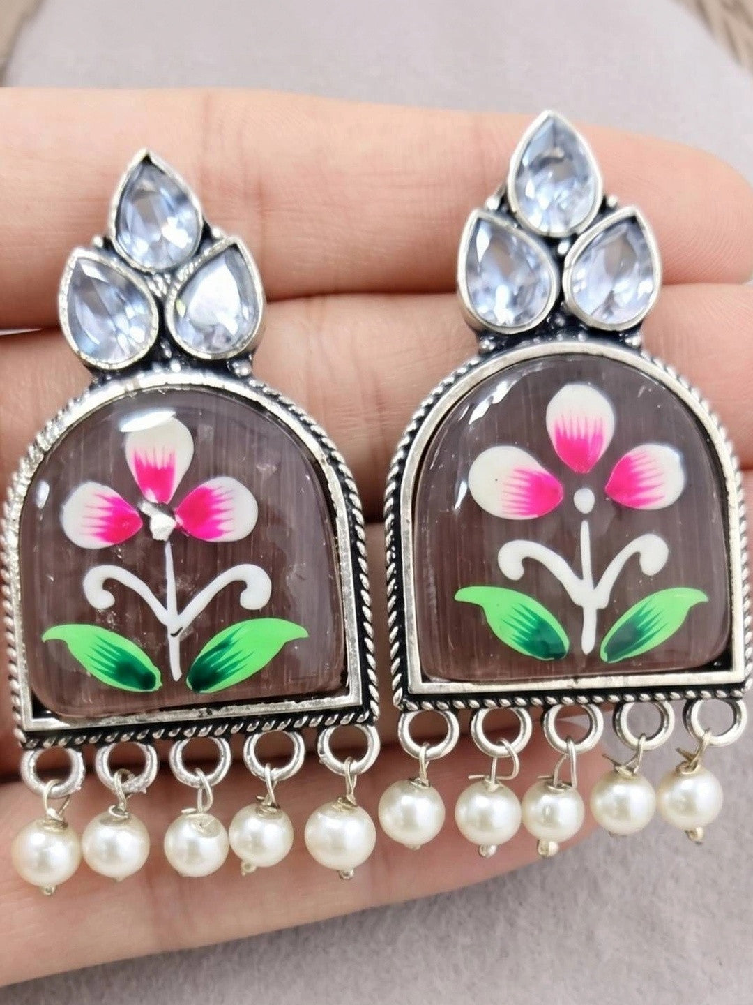 Close-up of hand-painted pink flower resin jhumka earrings held in a palm showing detail