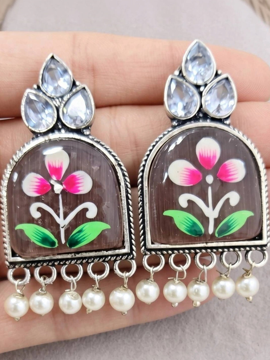 Close-up of hand-painted pink flower resin jhumka earrings held in a palm showing detail