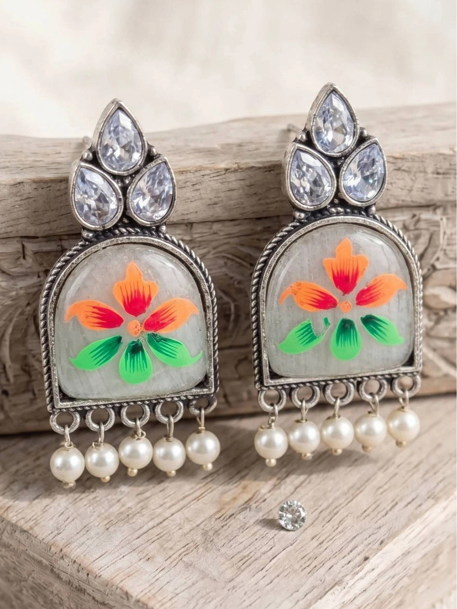 Pair of oxidised silver chandbali earrings propped against rustic wood with a loose crystal stone nearby