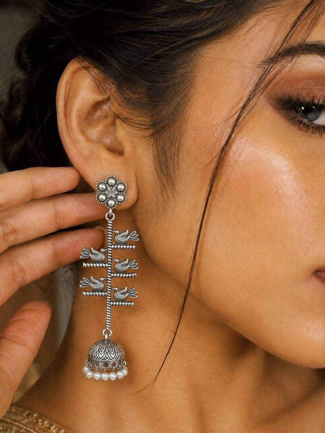 Oxidised silver bird jhumka earring worn on a woman's ear, showing full drop length with pearl fringe