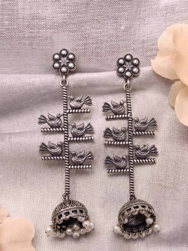 Pair of oxidised silver bird jhumka earrings laid flat on white fabric showing front detail of both pieces