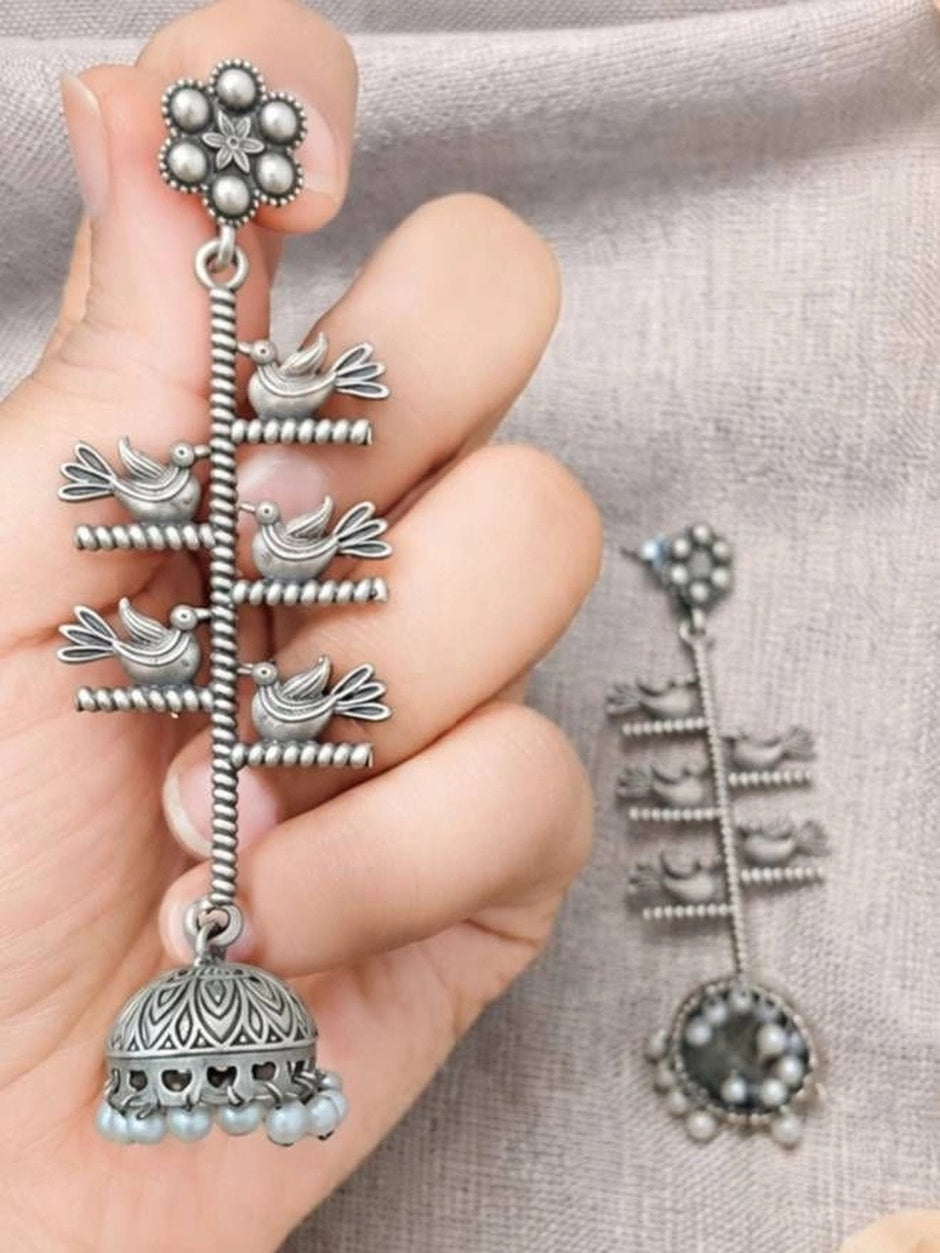 Single oxidised silver bird jhumka earring held in hand showing five bird motifs and domed pearl-fringed jhumka