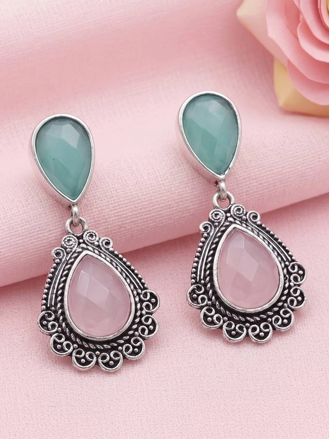 Pair of oxidised silver filigree teardrop earrings with teal and blush-pink stones on pink cloth