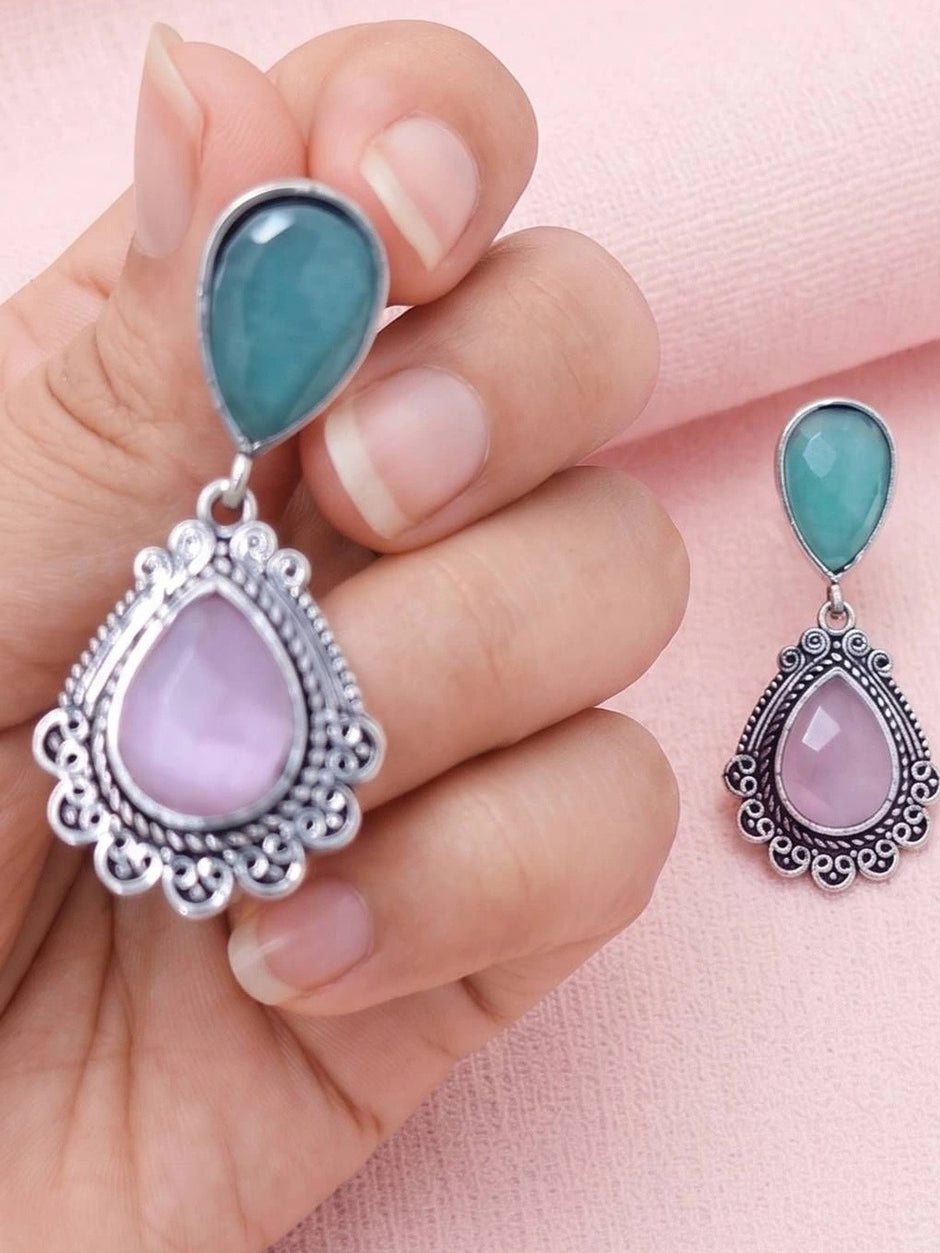 Hand holding one large oxidised silver teardrop earring beside a smaller matching earring on pink background
