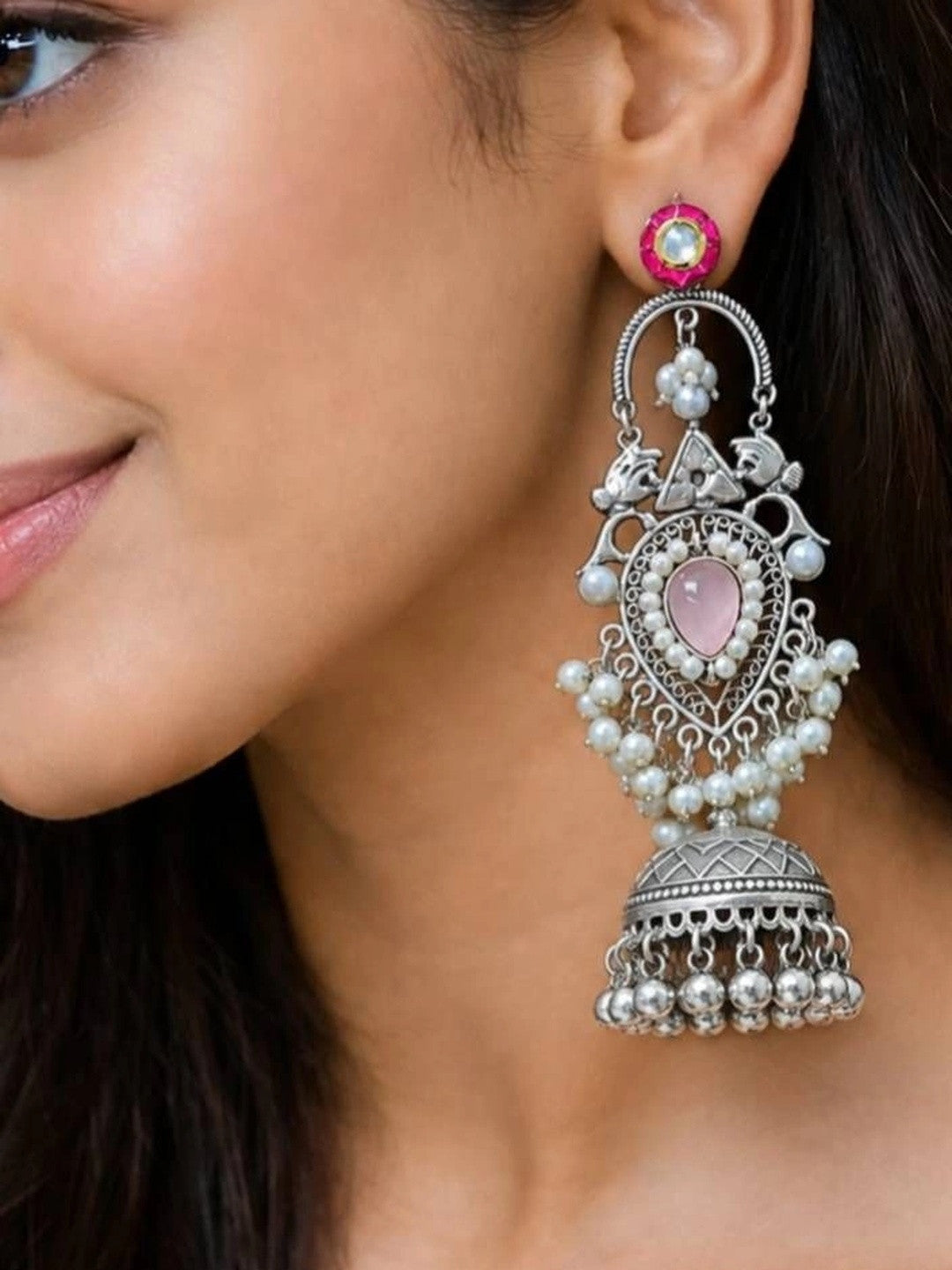 Close-up of oxidised silver teardrop jhumka with pink stone and pearl clusters worn on ear
