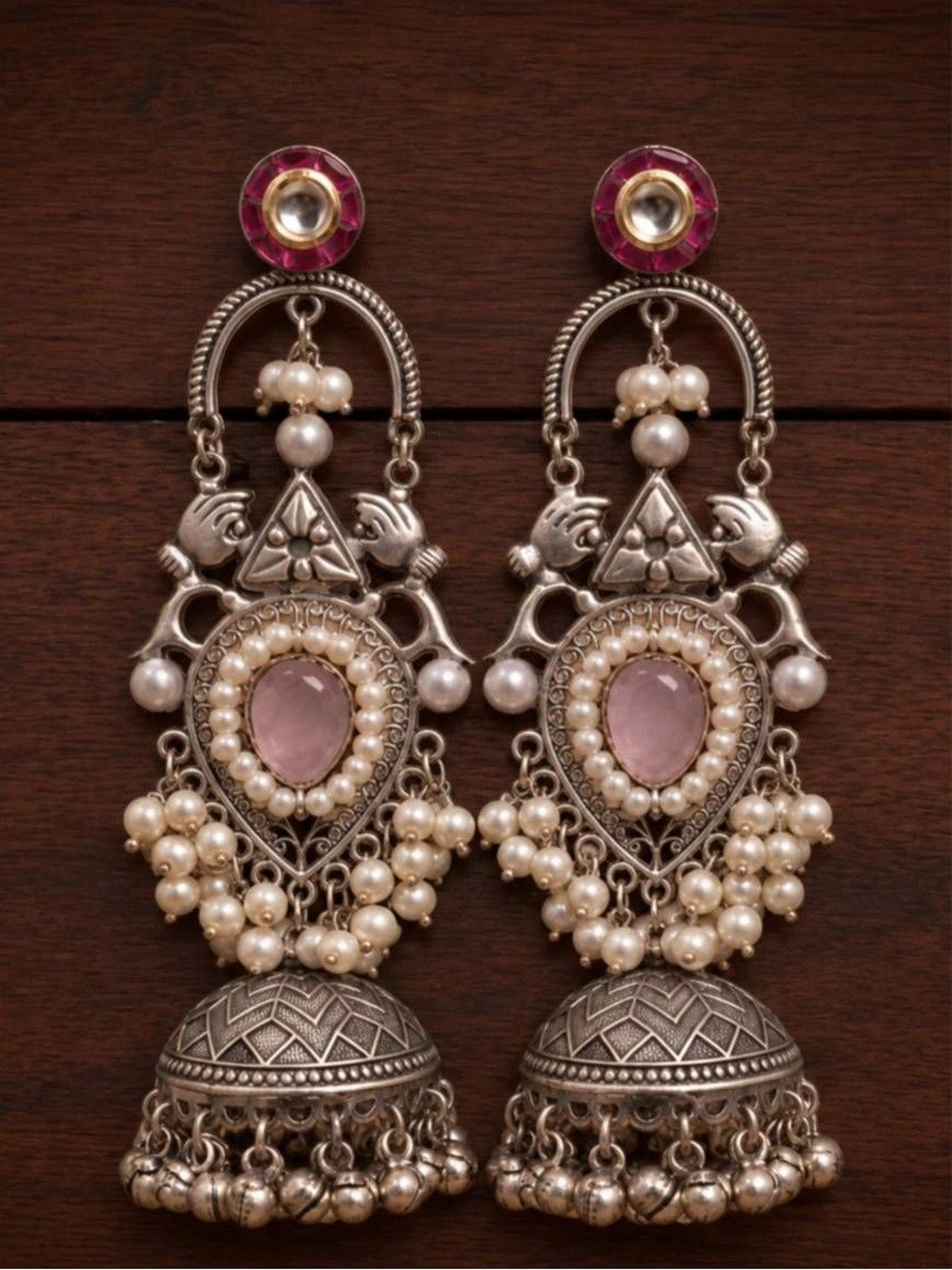 Pair of oxidised silver teardrop jhumka earrings laid flat on dark wooden surface