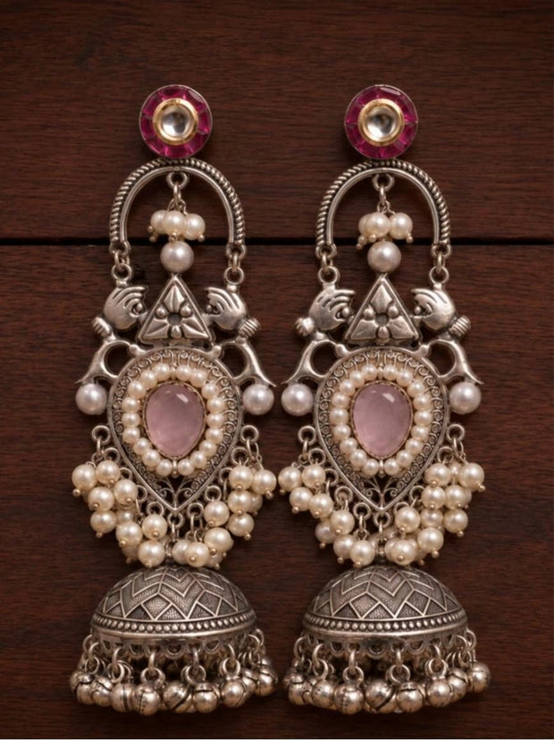 Pair of oxidised silver teardrop jhumka earrings laid flat on dark wooden surface