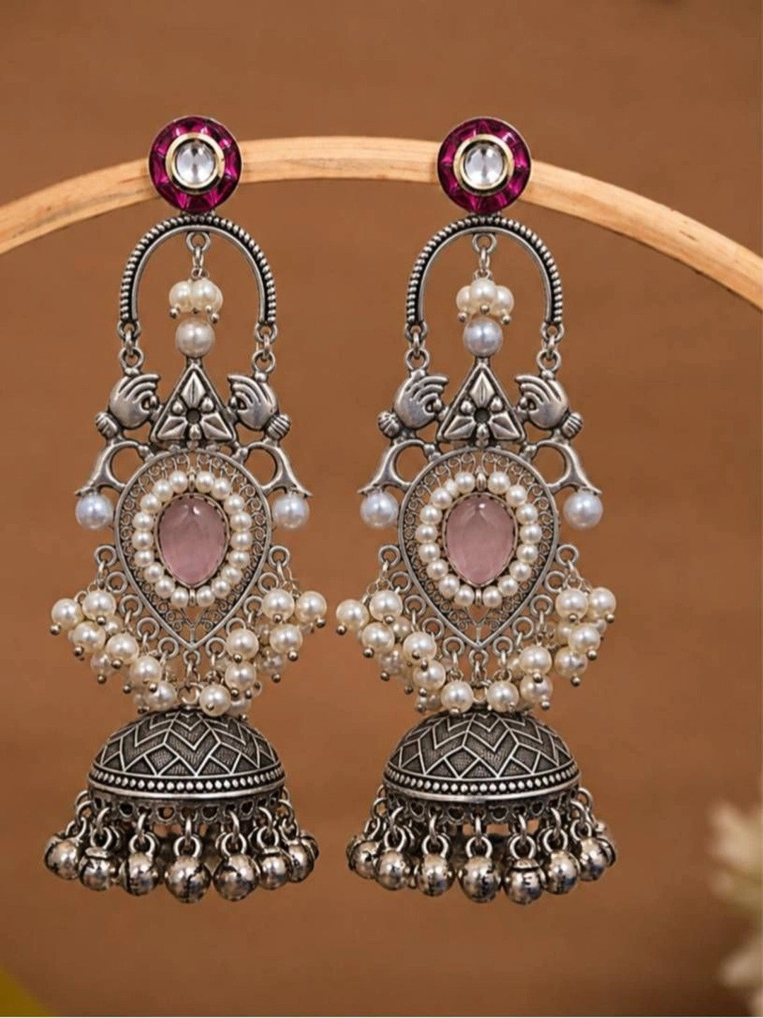 Pair of oxidised silver pearl jhumka earrings displayed on curved wooden prop