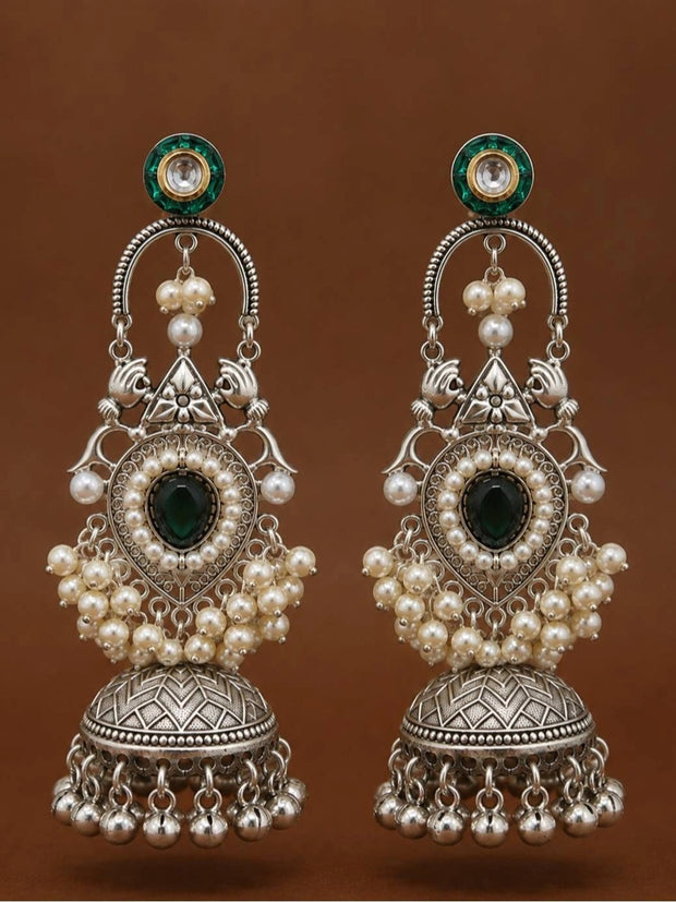 Pair of oxidised silver chandbali jhumka earrings with green kundan tops displayed against warm brown background