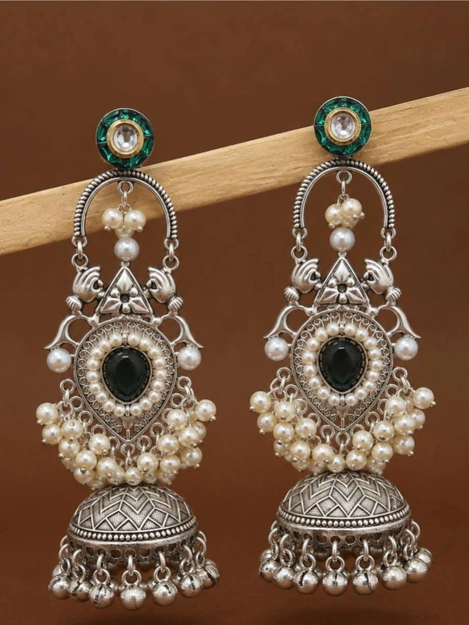 Two oxidised silver jhumka earrings with pearl-bordered teardrop stone hanging from a wooden rod