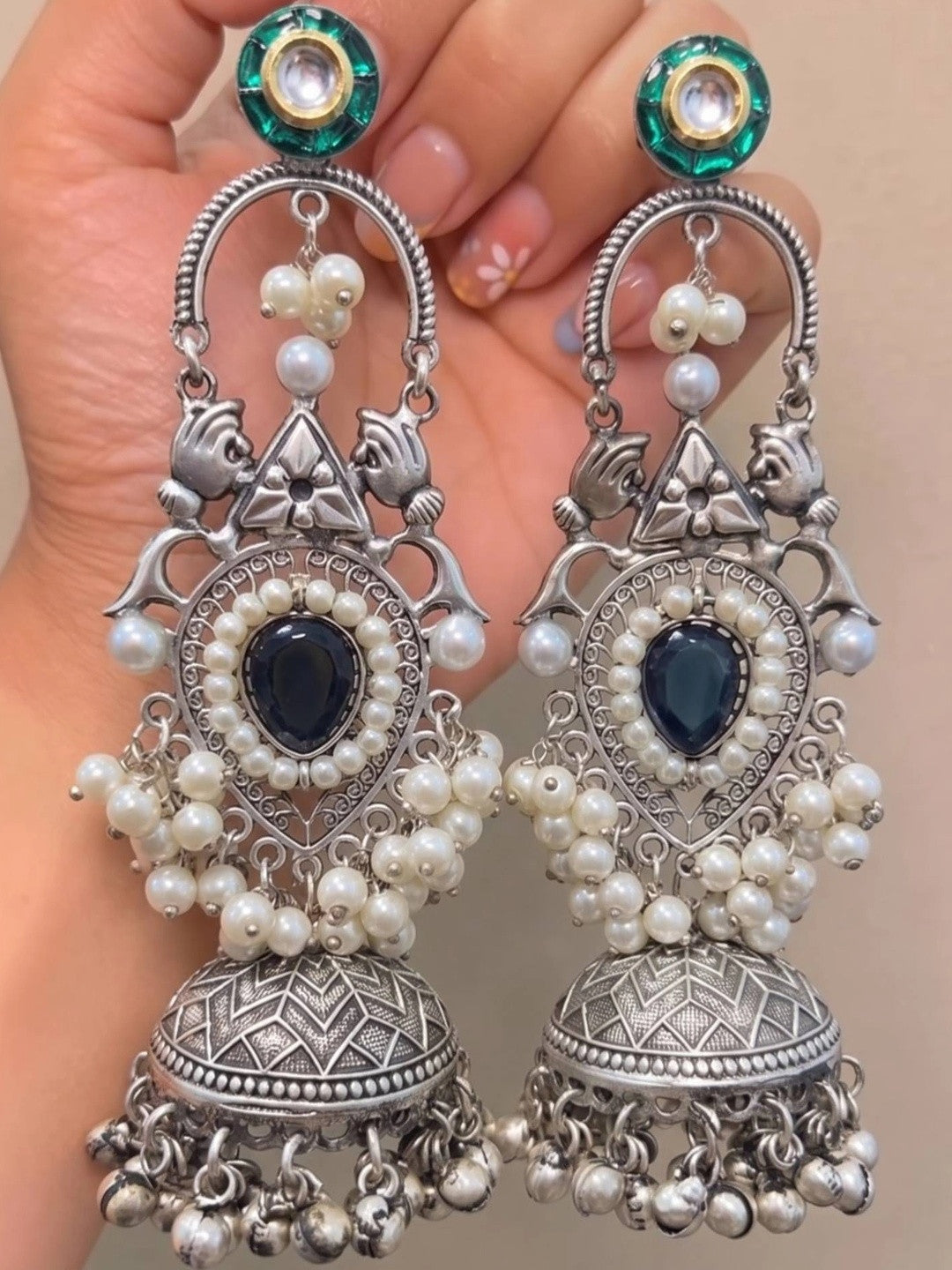 Close-up of a pair of oxidised silver pearl chandbali jhumka earrings held in a woman's palm