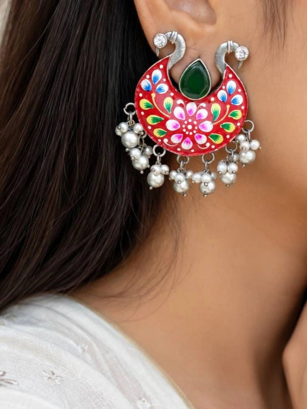 Red meenakari chandbali earring worn on ear showing peacock top and pearl fringe